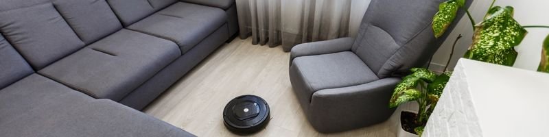 imagem robô aspirador de pó no meio da sala encima do piso entre os sofá